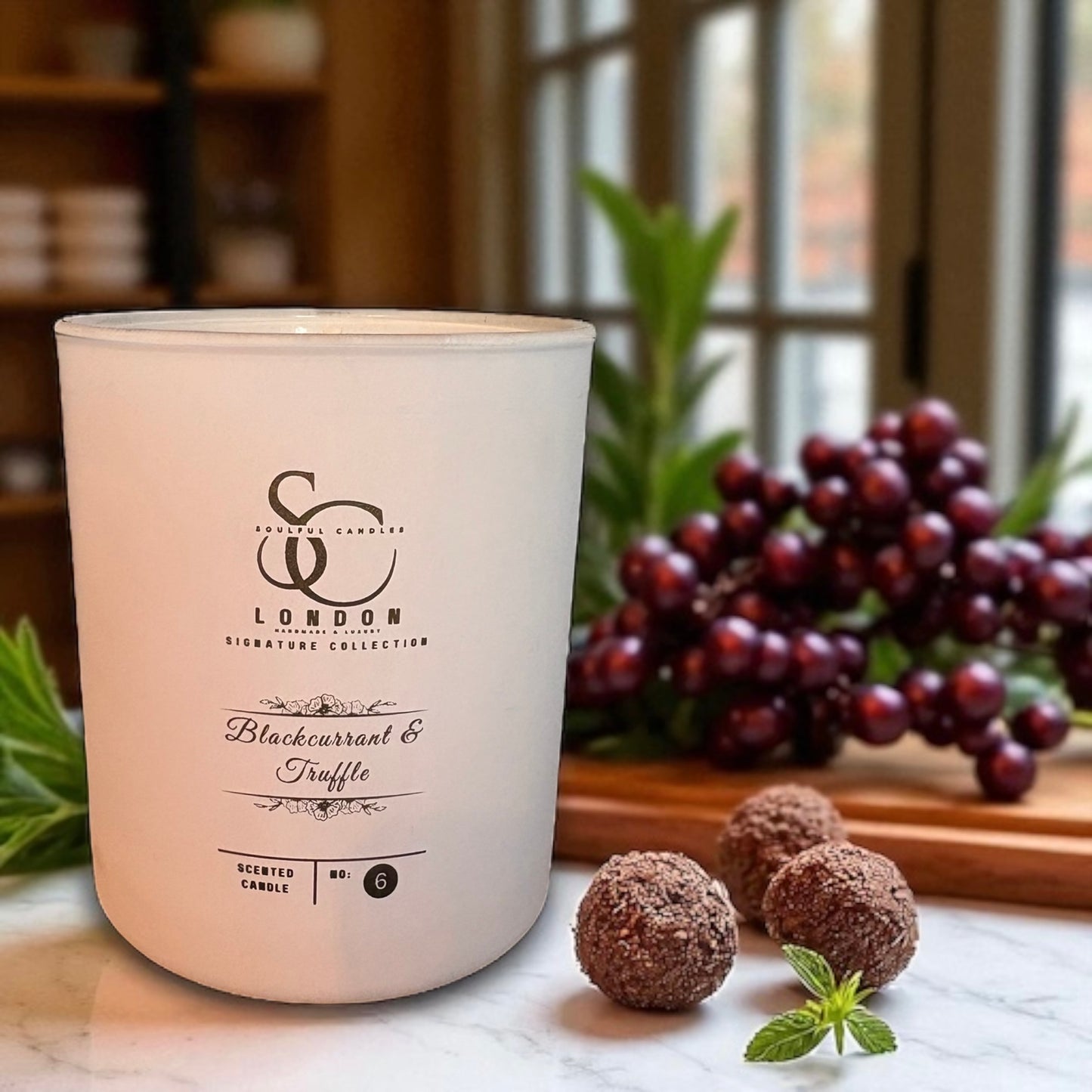 Candle with branding and product details on a marble surface with blackcurrants and truffles.
