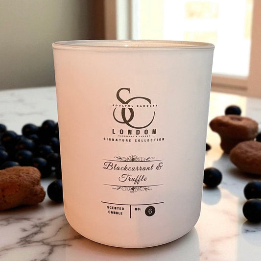White candle with branding on a marble surface with blackcurrants and truffles.