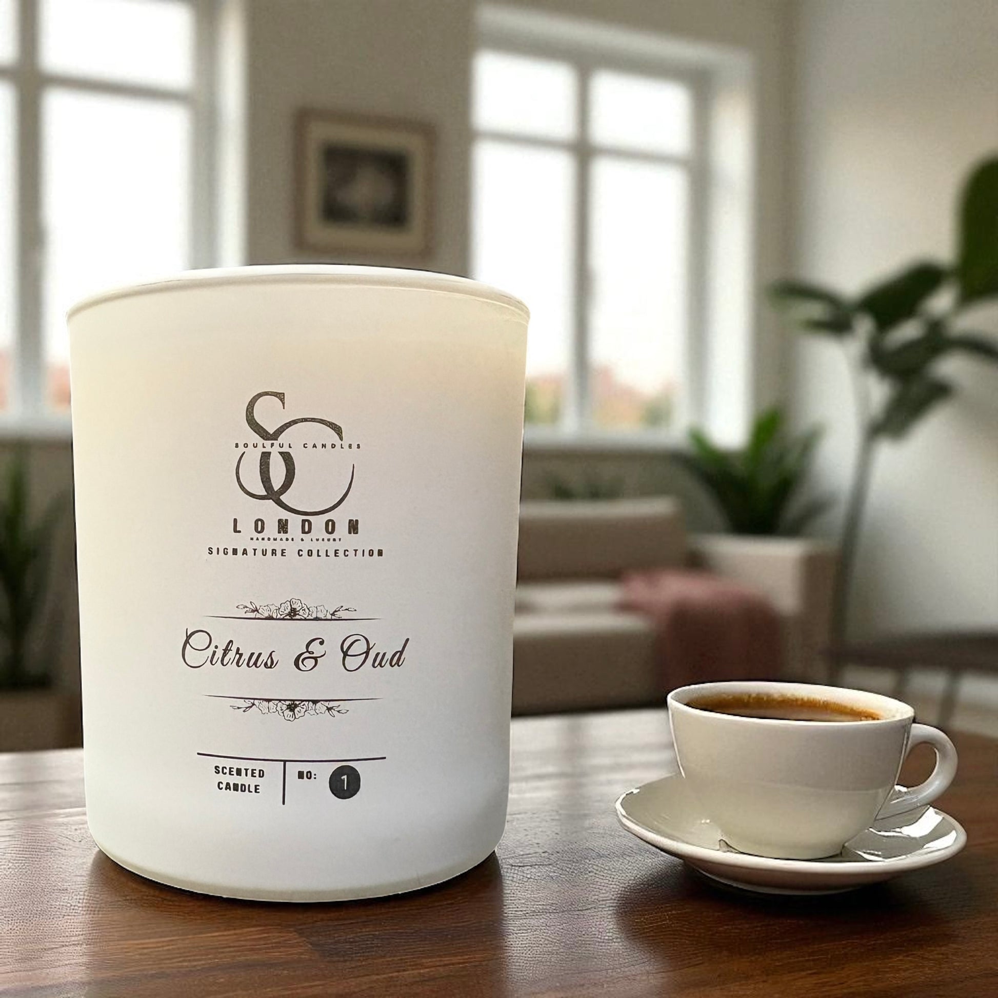 White candle labeled 'SCC London' with a cup of coffee on a wooden table in a room.