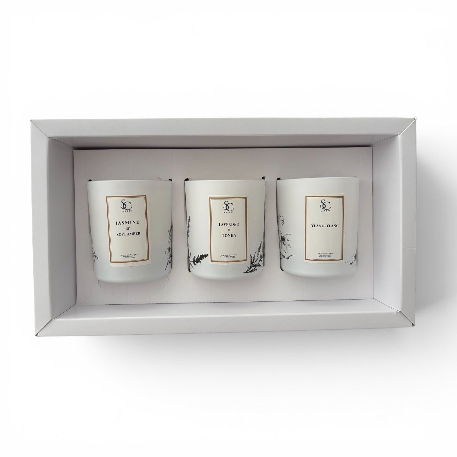 A three-scented soy candle gift set in a white rectangular box, featuring white glass jars with minimalist gold and black labels.
