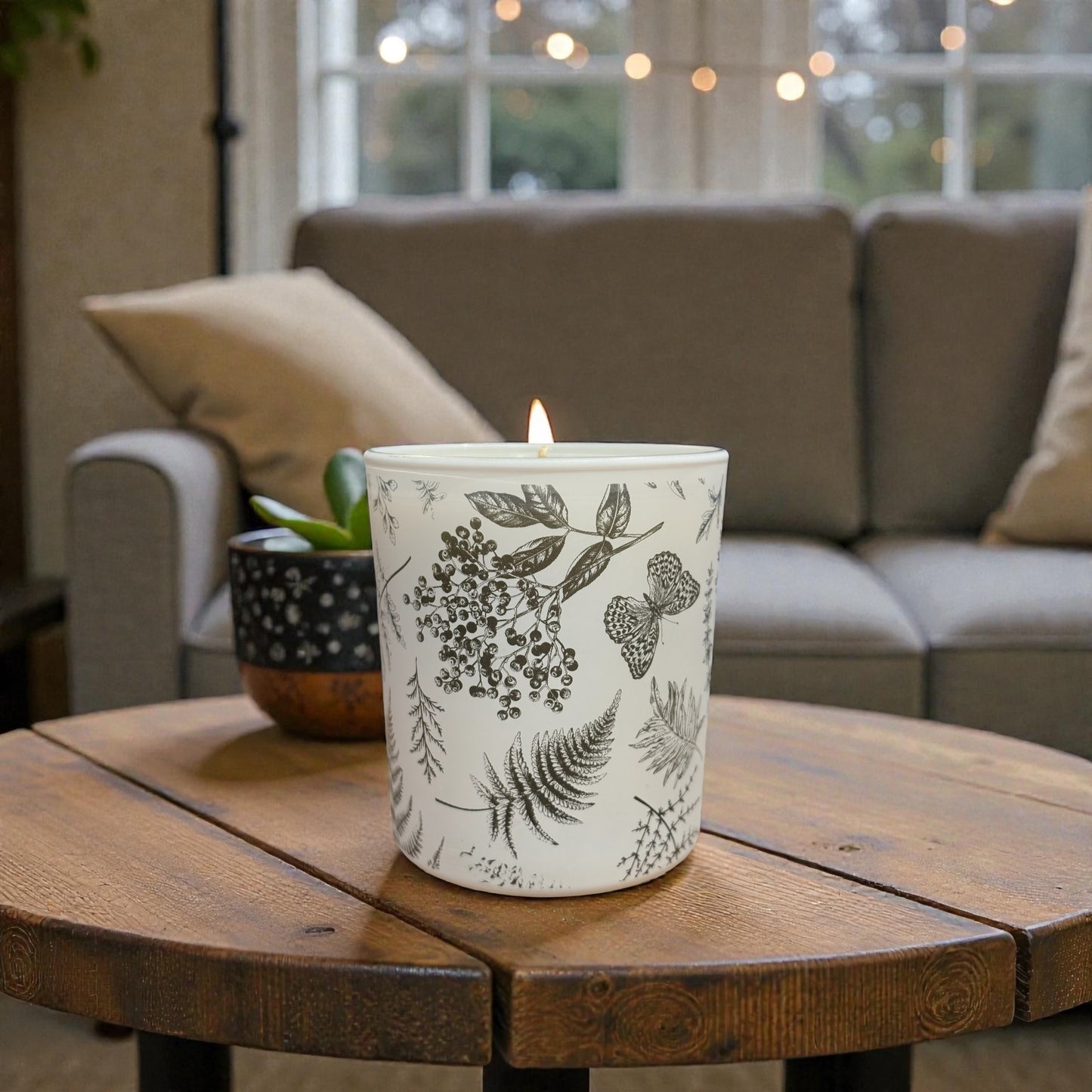 Candle with floral design on a wooden table in a cozy living room.